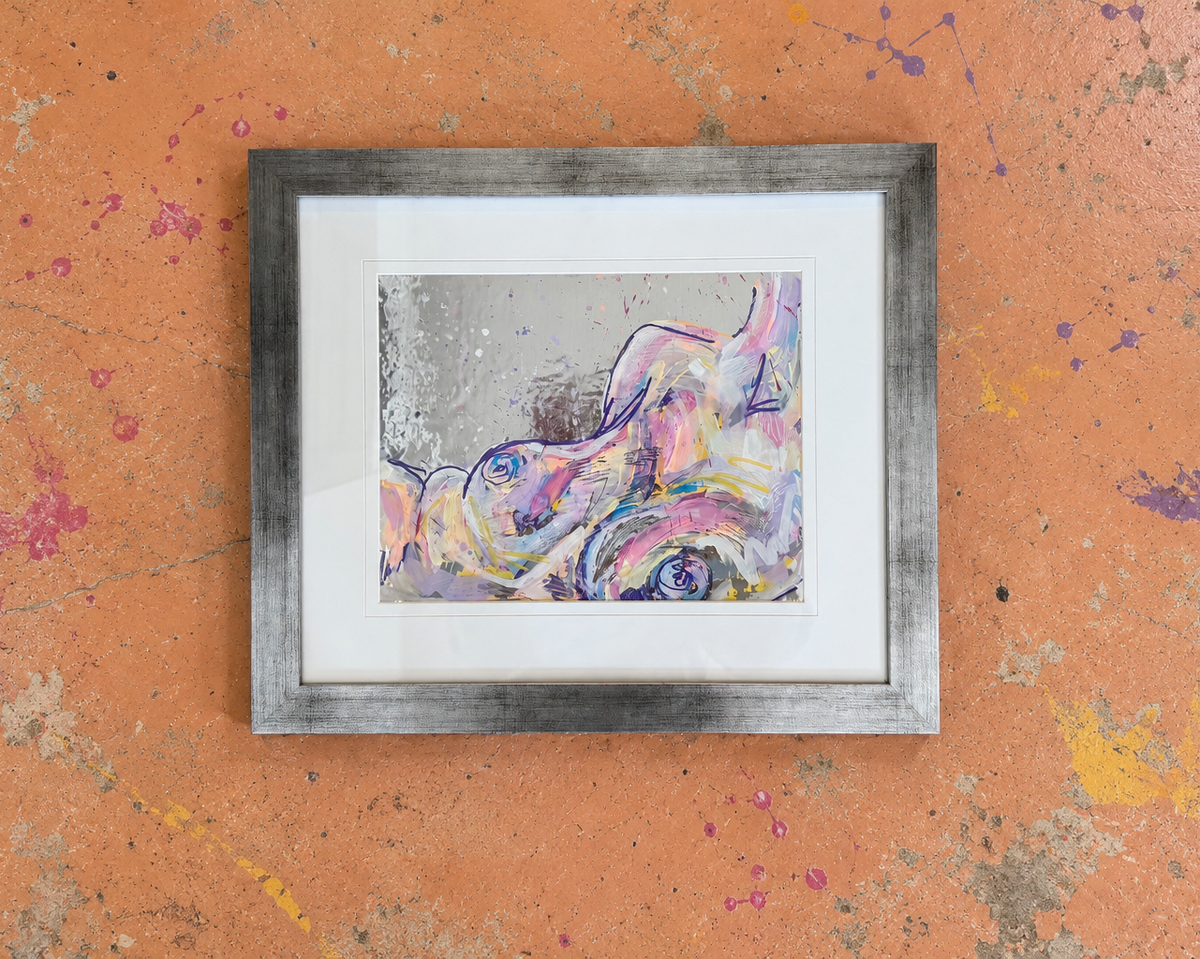 A framed abstract art painting featuring a colorful, painterly depiction of a reclining figure in shades of pink, purple, blue, and yellow on a textured gray background, housed in a distressed gray frame with a white mat, displayed against a textured orange wall with paint splatters.