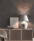 Load image into Gallery viewer, a white vase sitting on top of a dresser next to a lamp
